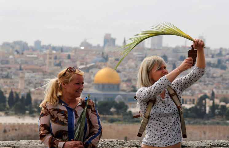 سيدتان مسيحيتان تقفان على جبل الزيتون في القدس وتحملان سعف نخيل احتفاء بأحد الشعانين